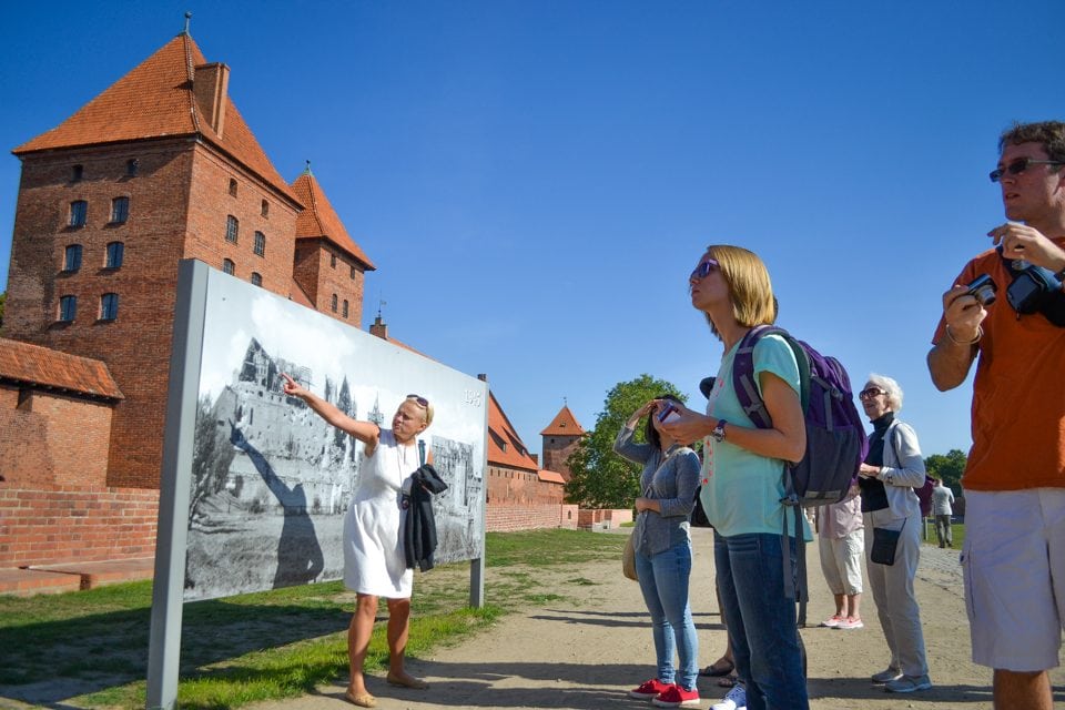 Guide, Magdalena Wieckiewiz, helps voyagers compare a photo of the Malbork Castle exterior at the end of World War II with its modern reconstruction. 