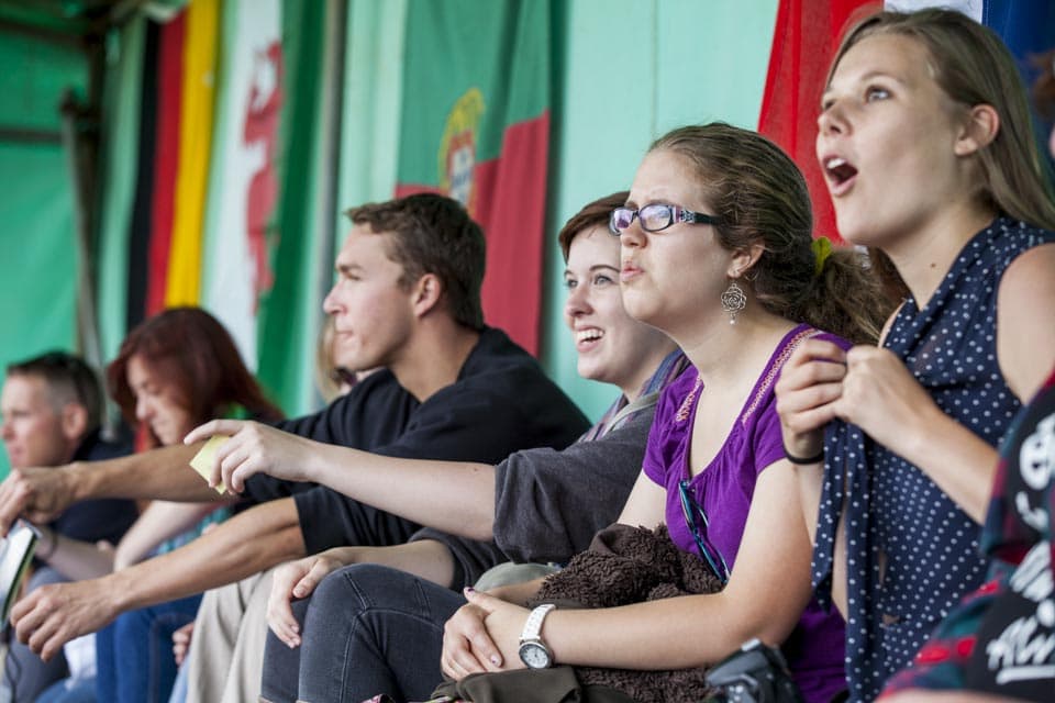 Students (from right) Kelsi Hamdorf of CU Boulder, Rebecca Kline of Stevens Institute and Kate McHargue of Colorado State University all have quite different reactions as they watched the show of muscles and brawn during the caber toss. 