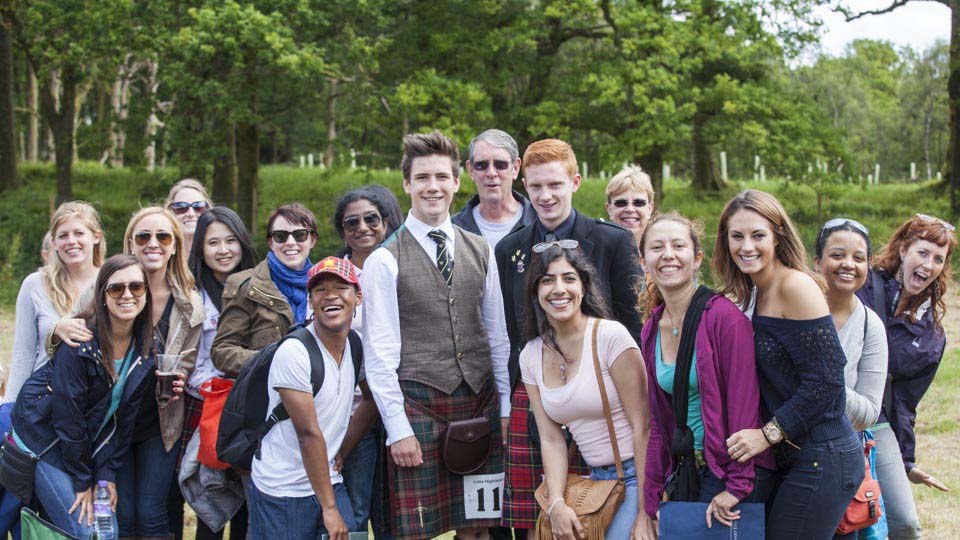 A group of students, staff, Academic Dean David Gies and his wife Janna, pose with two young Scottish men fresh out of an open bagpipe event. 