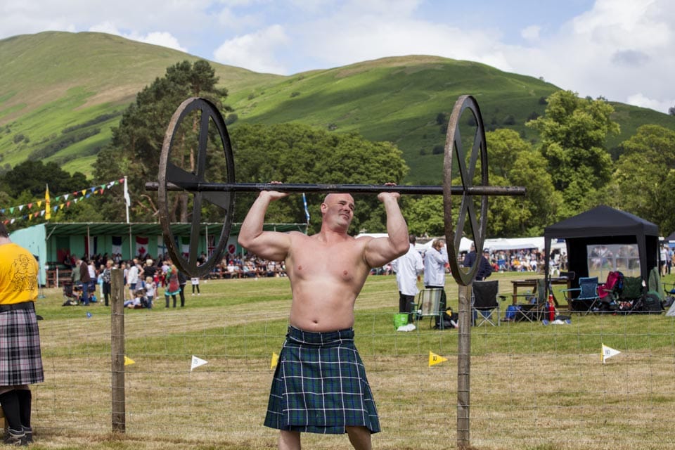 Heavy weight competitors warm up for the Viking Press event showing off kilts and muscles. Athletes lift this 250-pound weight above their head until their arms are fully extended. The athlete who can do the most repetitions within a 90 second time limit is the winner. 
