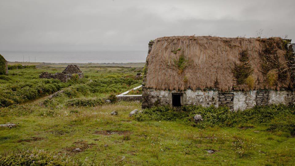After walking back down in the rain, the guide took a scenic route to the farthest west point of the island, pointing out thatch cottages that used to be the main housing style and are now just used as storage (the windows are all boarded up here) or can be seen in the distance as ruins. More modern housing has taken its place with stone roofing. 