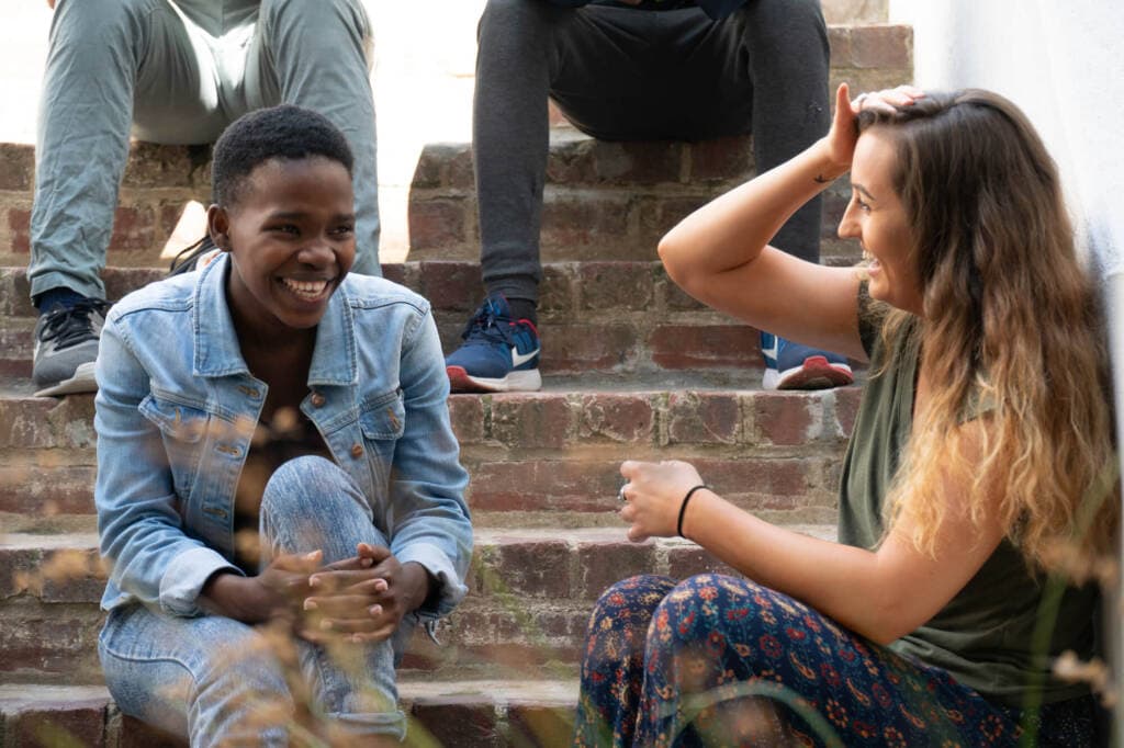 Two young people sit laughing together on a set of brick steps.