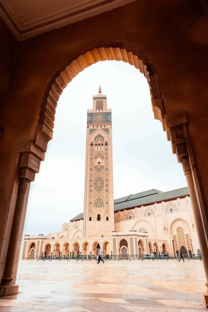 The iconic white-and-blue-tiled tower of the Hassan II Mosque, as seen through a carved stone archway.