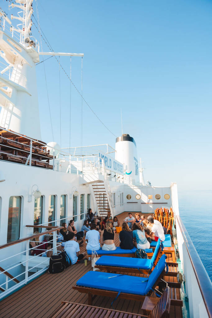 A group of students sitting in a circle on the deck of a boat engaged in a discussion.