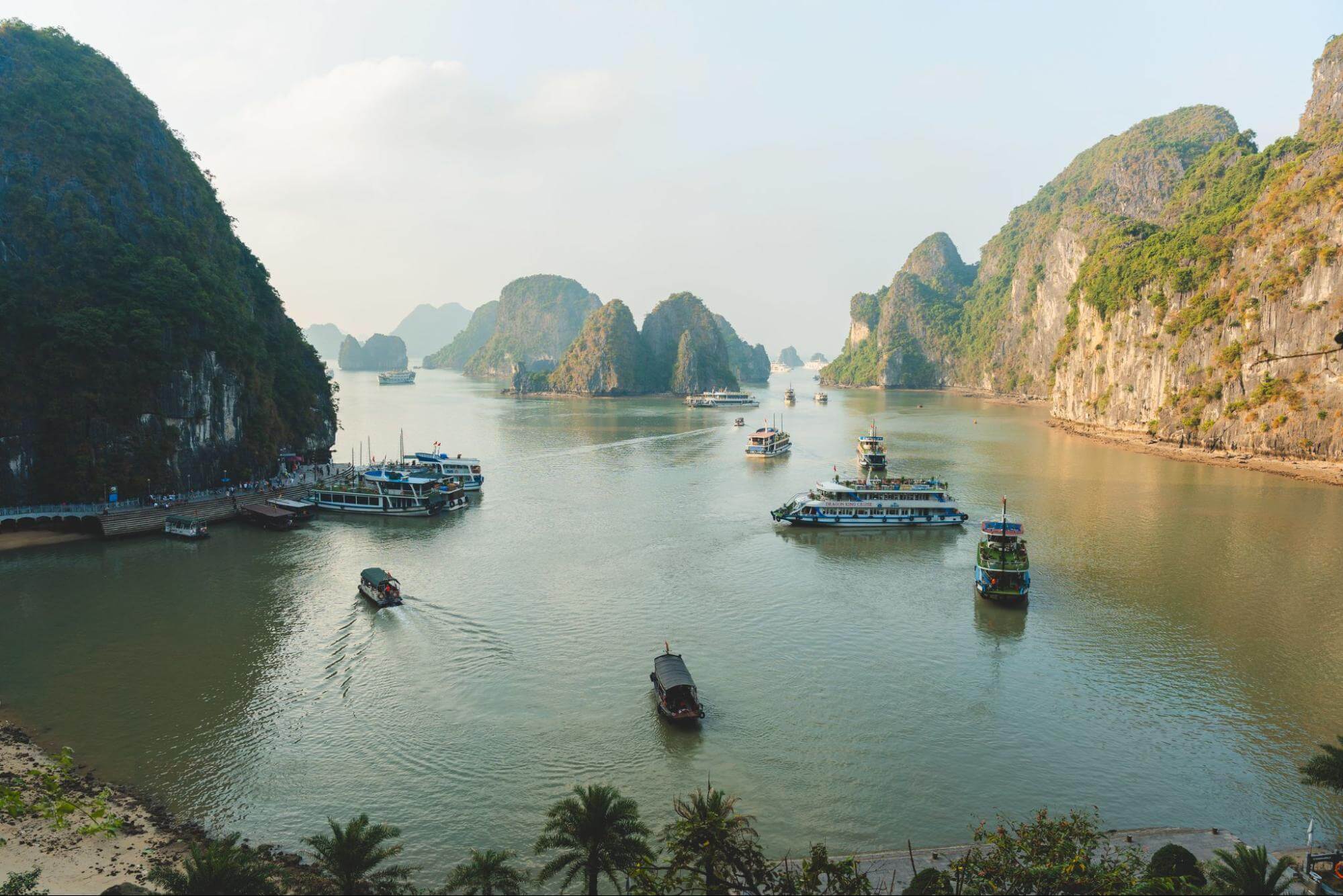 An aerial shot of a tranquil Hạ Long Bay, with boats of various sizes sailing between towering karst rock formations.