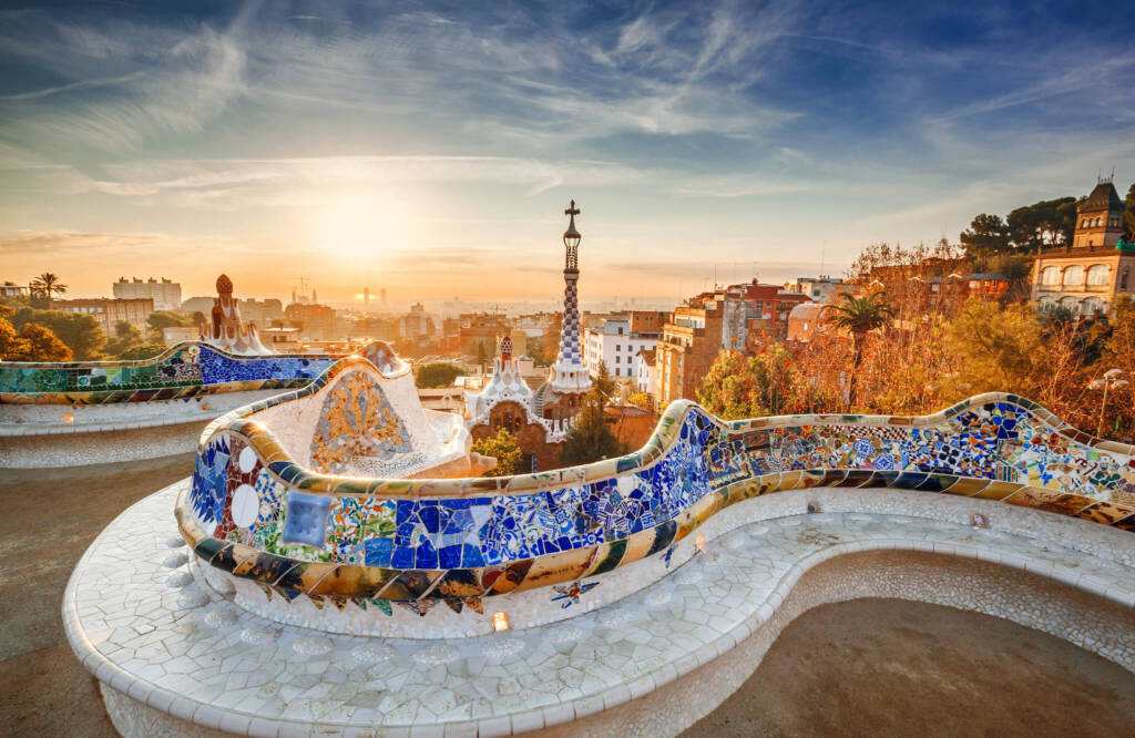 View of Barcelona at sunrise from a colorful mosaic balcony in Park Güell. 