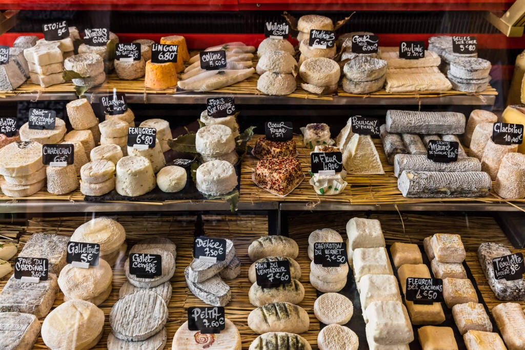 A large selection of different French and Italian cheeses on the counter of a small store in a Parisian market.