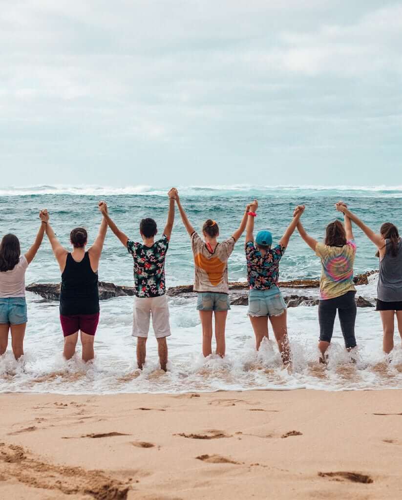People on the beach looking at the ocean holding hands above their head.